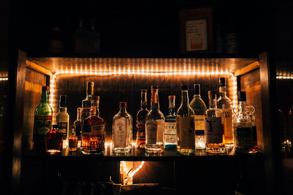 A stylish arrangement of various liquor bottles beautifully illuminated on a shelf in a dimly lit bar setting.