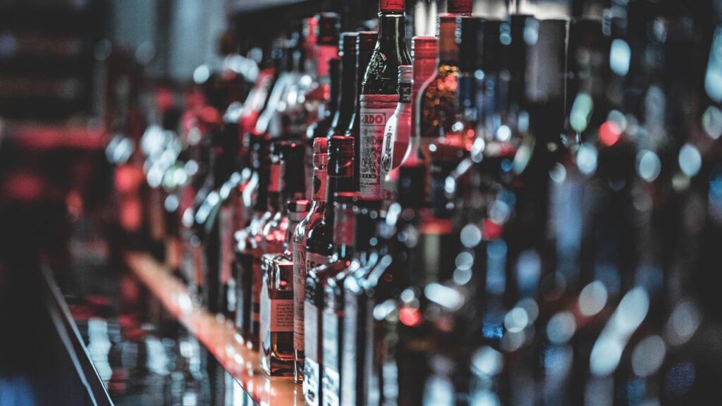 Blurred view of assorted alcohol bottles lined up on a bar shelf indoors.