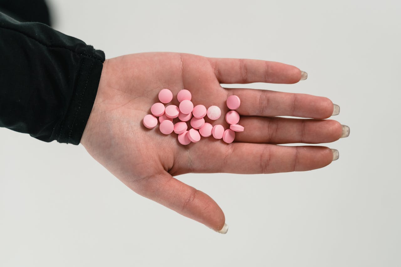 A close-up of a hand holding pink pills, highlighting addiction and healthcare themes.